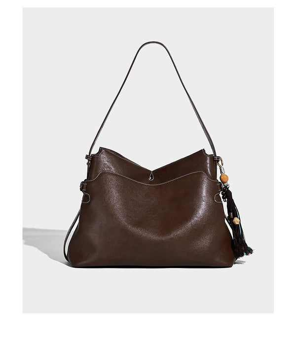Large slouchy leather-look hobo tote bag with open top, adjustable shoulder strap, and colorful tassel bead charm, detail