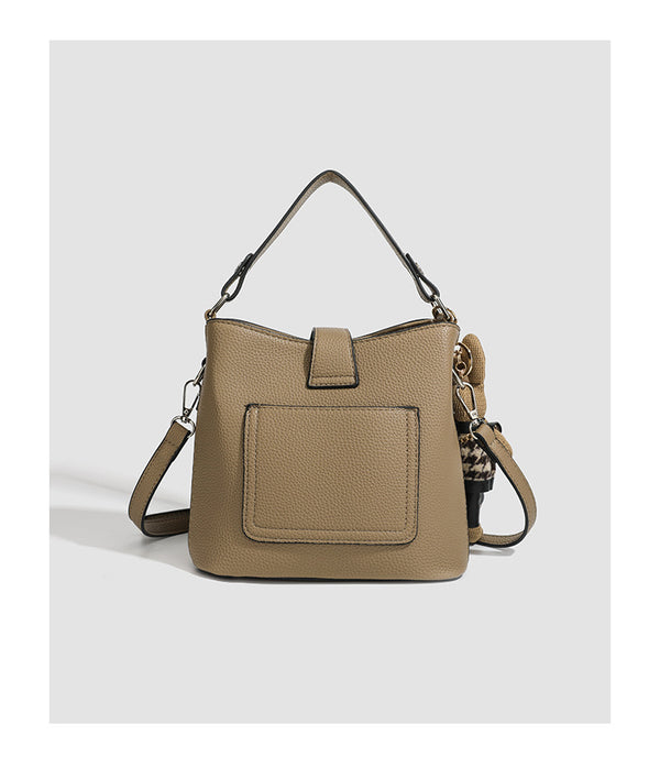 Structured taupe pebbled-texture bucket bag with top handle, silver ring hardware, tab-and-button closure, and knit bunny