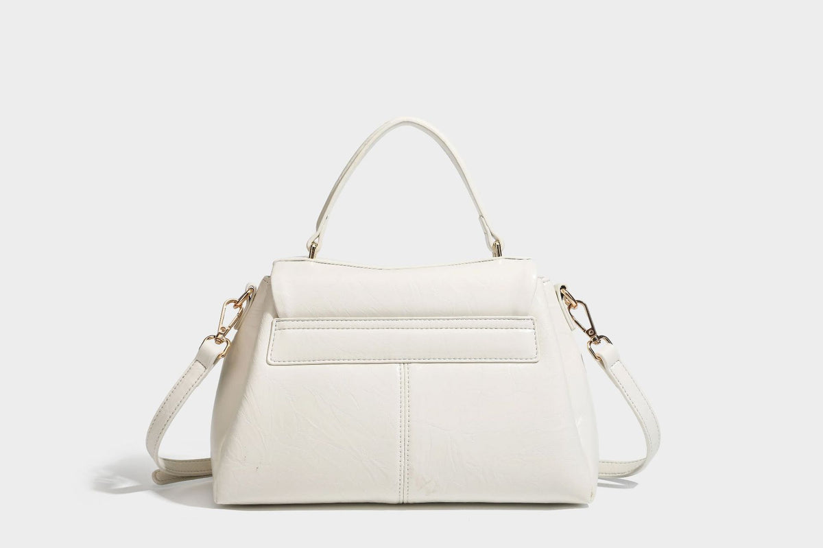 Structured black satchel bag with glossy crinkled leather-look finish, gold-tone emblem flap closure, slim top handle, and