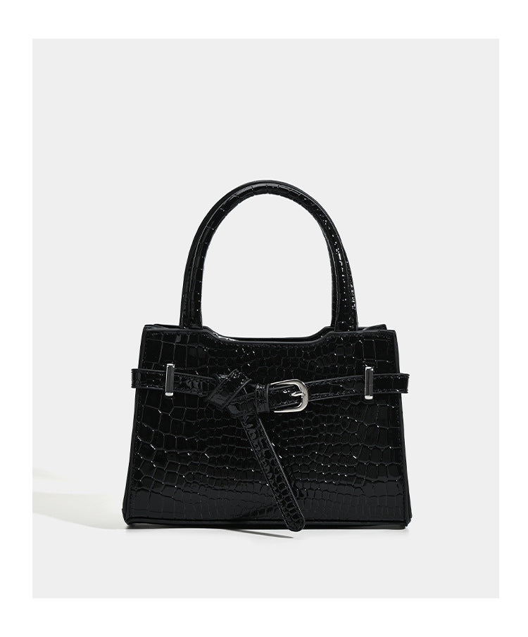 Small structured trapezoid mini top-handle bag with front belt-knot buckle detail and glossy leather-look finish, detail view