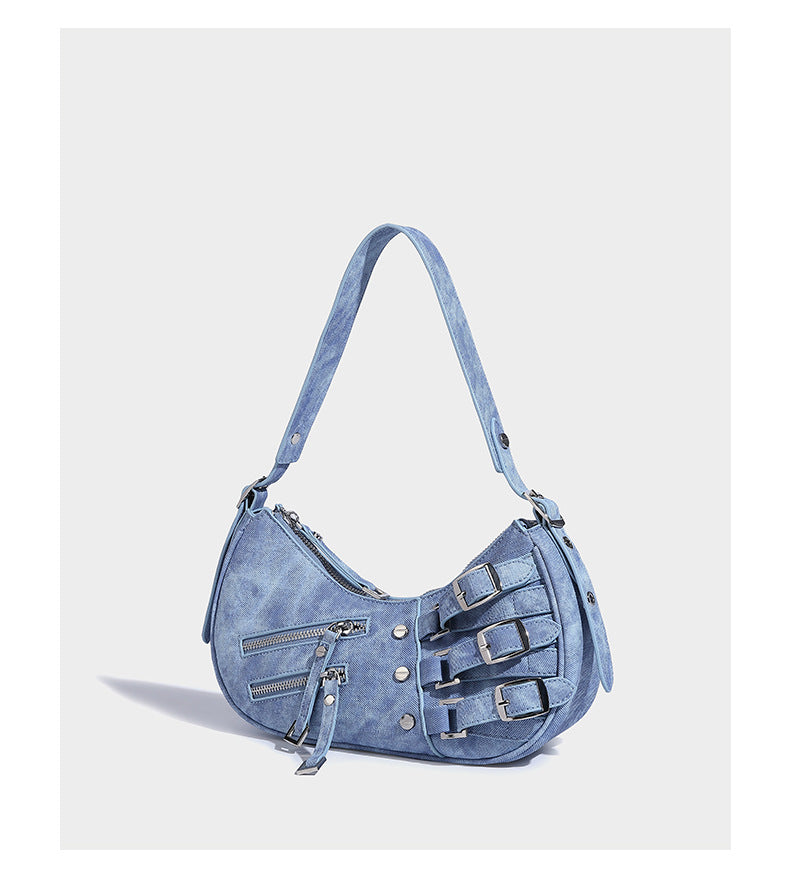 Crescent shoulder bag in washed blue denim-look PU with stacked buckle straps, front zip pocket, and silver-tone hardware