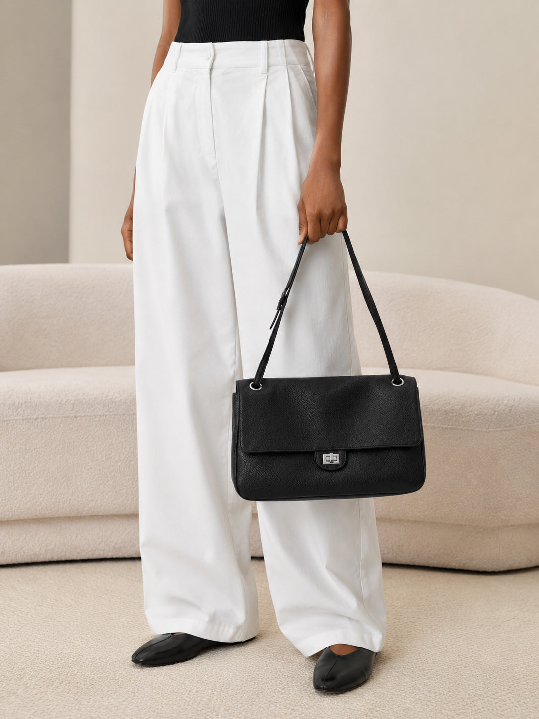 Structured black flap shoulder bag with pebbled texture, silver-tone turn-lock closure, and adjustable single shoulder strap