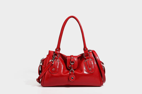Glänzende, geknautschte Barrel-Satchel mit zwei oberen Tragegriffen, vorderem Klappen-Riemen-Panel, Ring- und Nietenbeschlägen sowie einem abnehmbaren