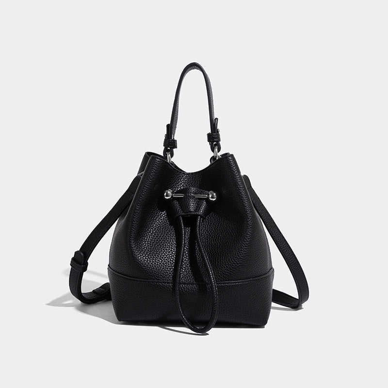 Small two-tone pebbled drawstring bucket bag with tan contrast base, metal toggle hardware, short top handle, and detachable