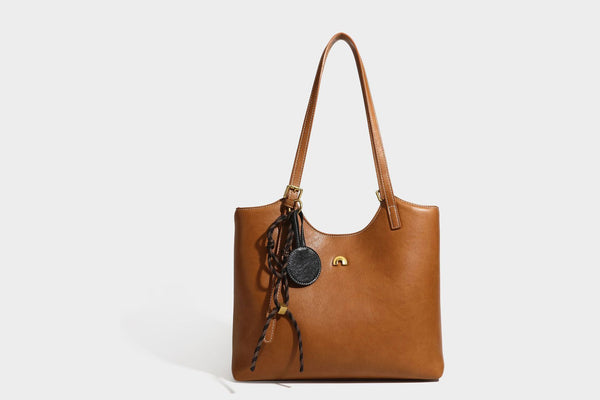 Structured smooth leather-look tote bag with long shoulder strap, gold-tone hardware, and hanging tassel-coin charm, detail