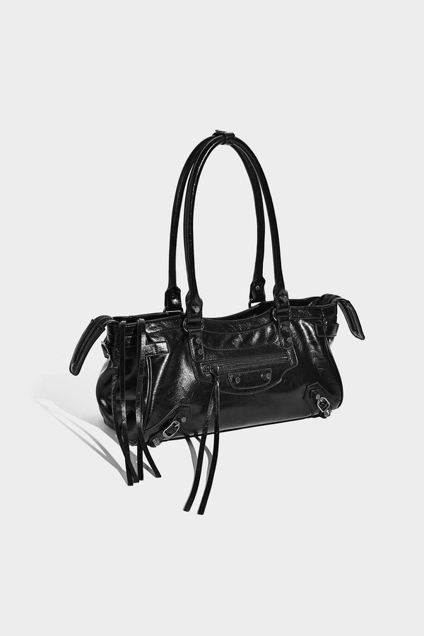 Längliche Schultertasche in Zylinderform mit glänzender Lederoptik, silberfarbenen Nietenbeschlägen, seitlichen Quasten und mehreren außenliegenden Reißverschlüssen