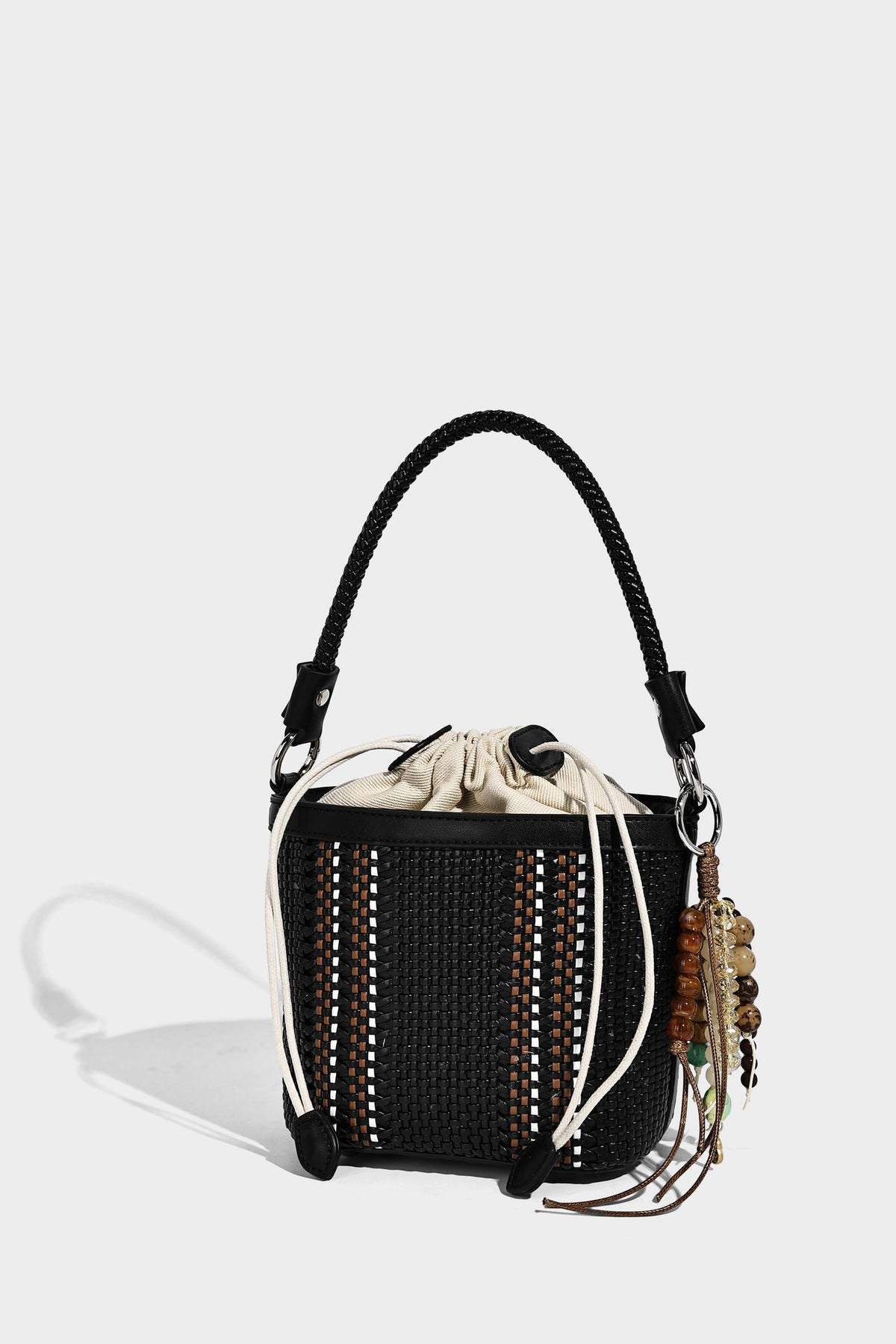 Small woven bucket bag with drawstring top, braided handle, detachable crossbody strap, and silver-tone ring hardware, detail