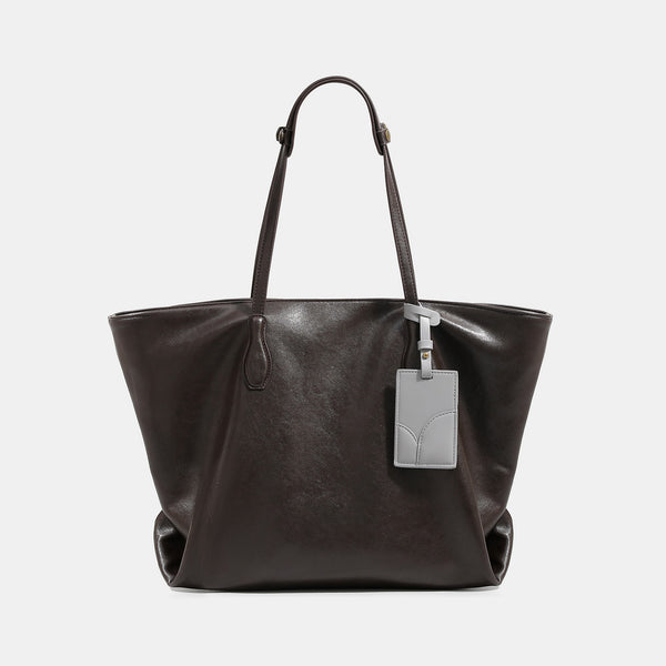 Large soft trapezoid tote bag with leather-look finish, dual shoulder straps, and gray hanging card tag, detail view 6