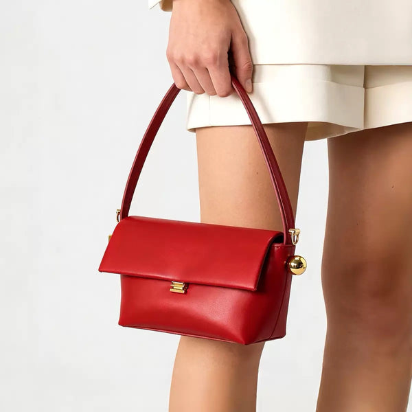 Structured trapezoid flap shoulder bag in red leather-look finish with gold-tone turn-lock clasp, sphere accent, and curved