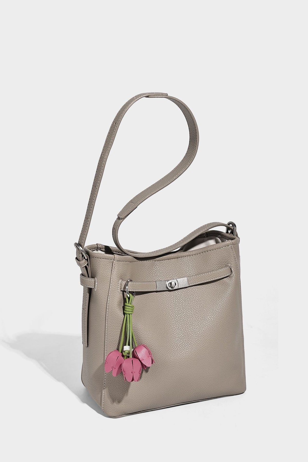 Soft-structured pebbled bucket shoulder bag with front turn-lock strap detail, adjustable strap, and hanging floral tassel