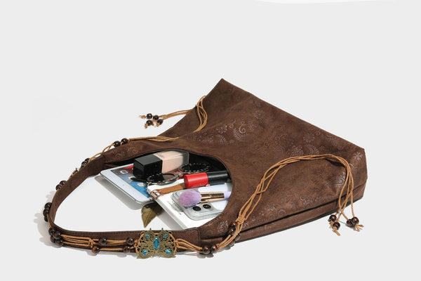 Slouchy boho hobo shoulder bag in embossed brown suede-look finish with beaded strap, cord tassels, and brass-tone leaf