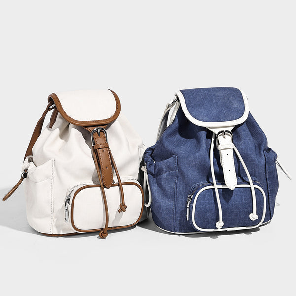 Compact denim drawstring backpack with white leather-look piping, flap-top buckle closure, front zip pocket, and silver-tone