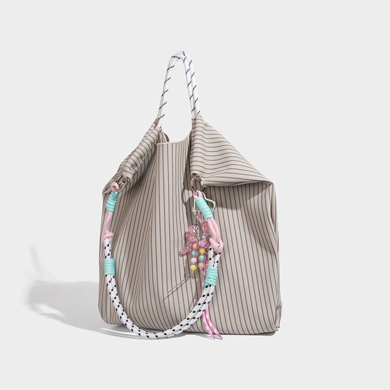 Slouchy pinstripe tote bag with braided rope handles, metal ring hardware, and colorful knotted rope charm, front view