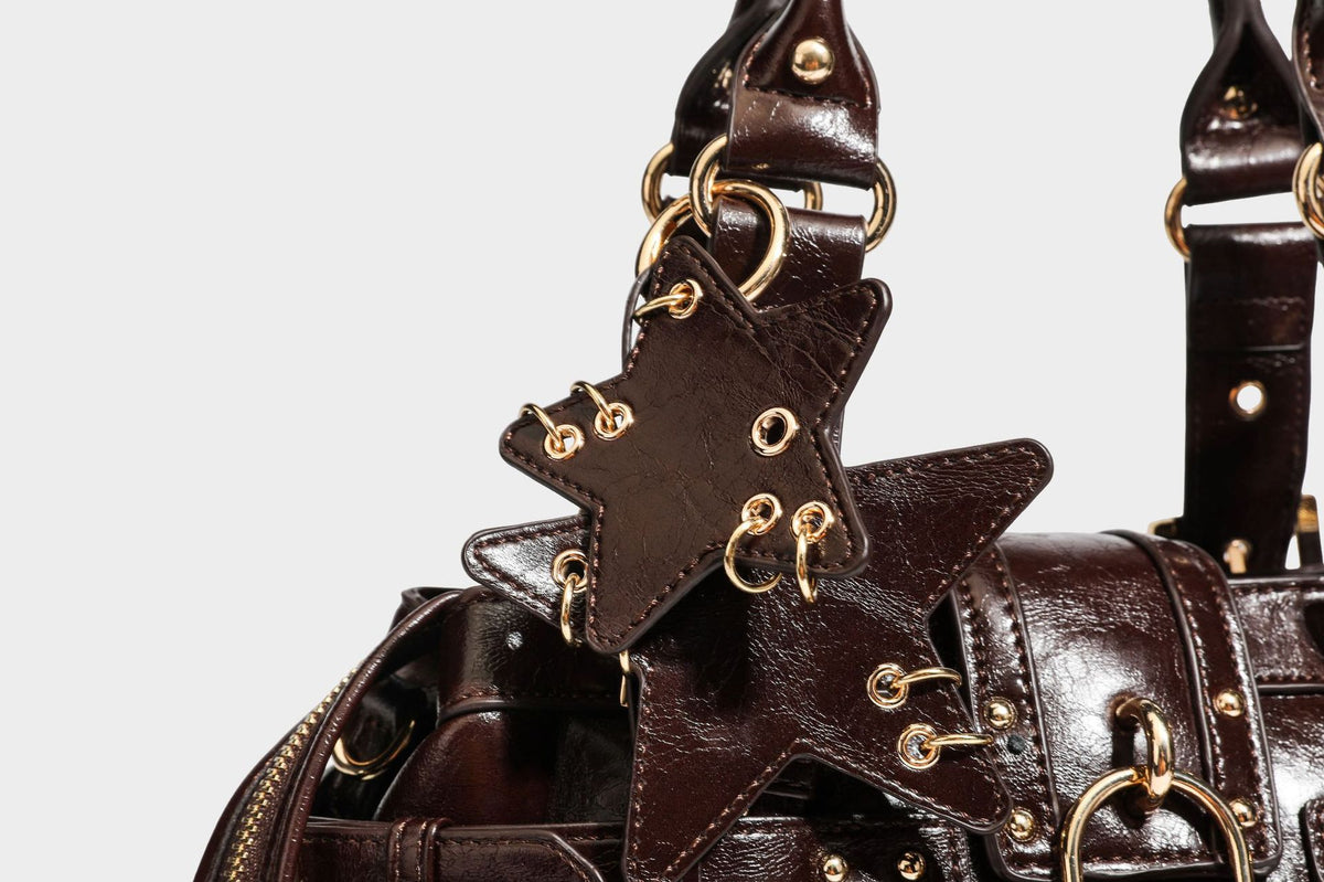Structured leather-look satchel bag with heart padlock charm, star charm, gold-tone buckle hardware, dual top handles, and