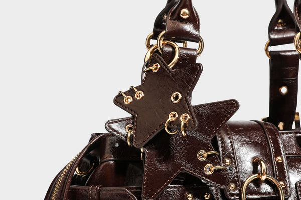 Structured leather-look satchel bag with heart padlock charm, star charm, gold-tone buckle hardware, dual top handles, and