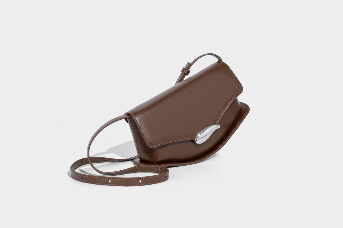 Small structured saddle bag with glossy leather-look finish, angular flap front, silver-tone metal clasp, and slim