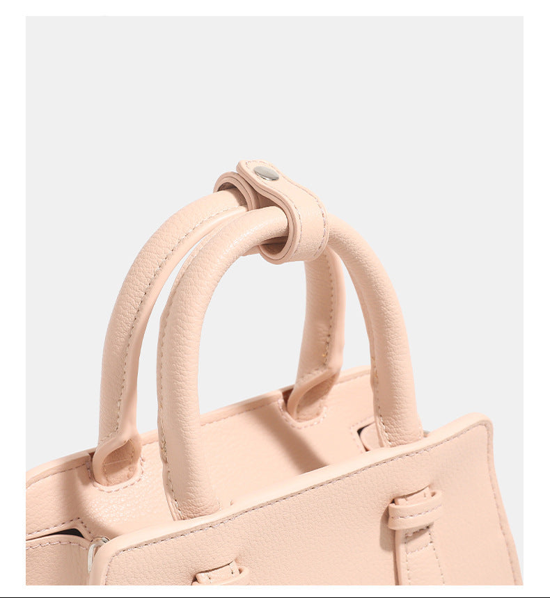 Small structured trapezoid top-handle bag in pebbled matte finish with decorative strap tabs, twin knotted handles, and