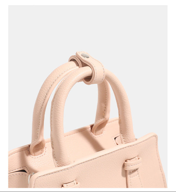Small structured trapezoid top-handle bag in pebbled matte finish with decorative strap tabs, twin knotted handles, and