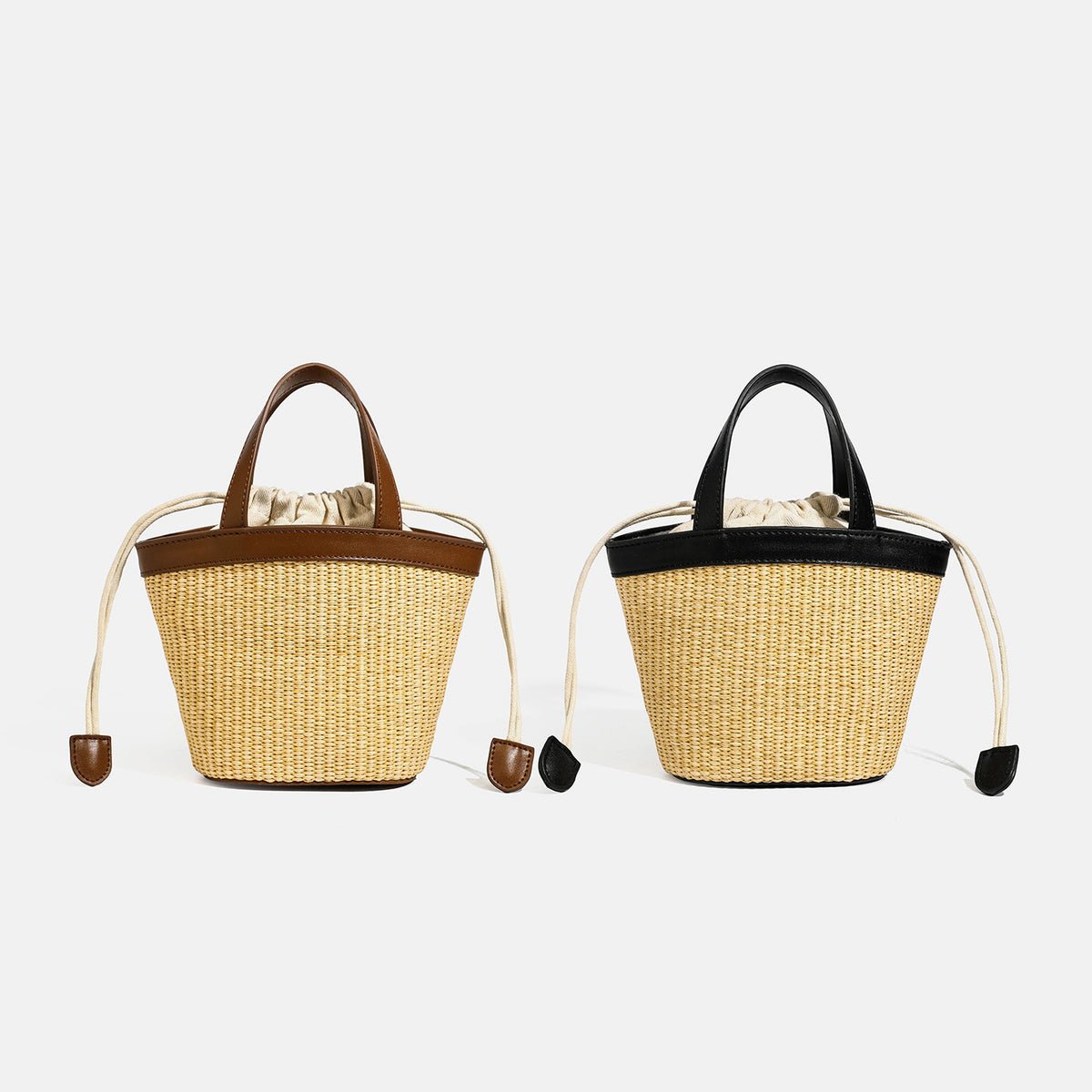 Small woven straw bucket bag with leather-look black trim, twin top handles, cream drawstring liner, and side cord closures