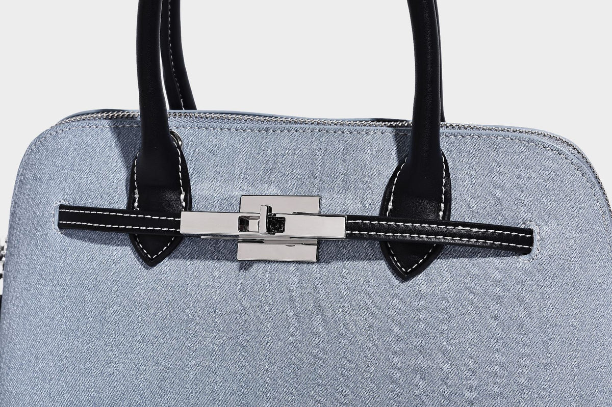 Compact structured satchel in light blue denim-look fabric with black leather-look trim, silver turn-lock closure, rolled
