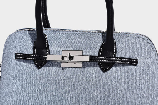 Compact structured satchel in light blue denim-look fabric with black leather-look trim, silver turn-lock closure, rolled