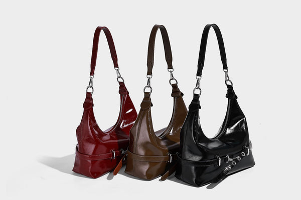 Glossy black slouchy hobo shoulder bag with silver-tone hardware, belt-style grommet strap at base, and long adjustable
