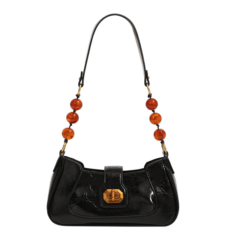 Compact glossy crinkled baguette shoulder bag with amber resin bead strap accent and gold-tone turn-lock closure, detail view