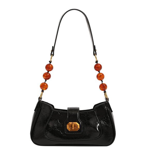 Compact glossy crinkled baguette shoulder bag with amber resin bead strap accent and gold-tone turn-lock closure, detail view