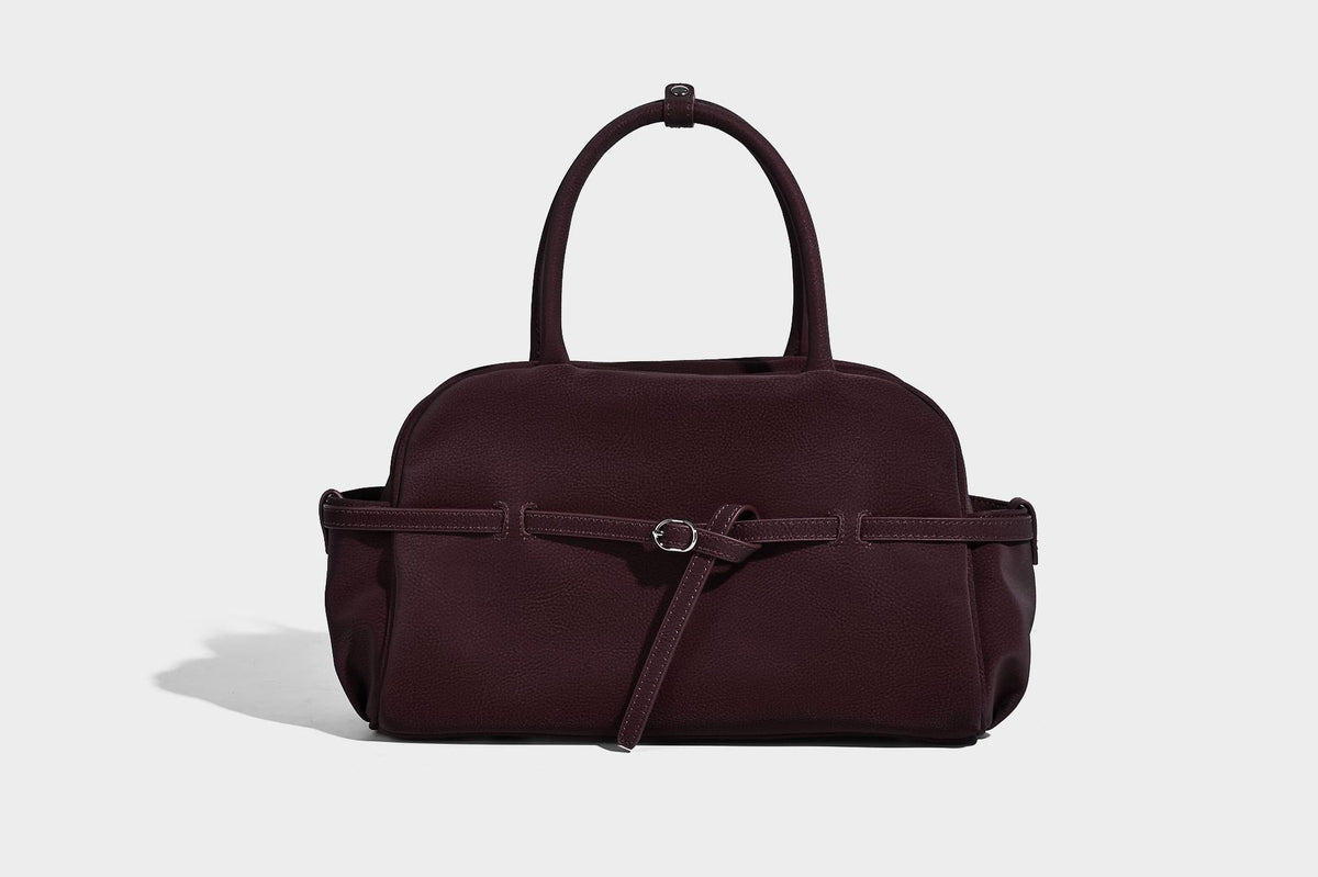 Strukturierte Henkeltasche aus mattem, genarbtem Material mit umlaufendem Riemen und Ringbeschlägen, zwei oberen Tragegriffen und abnehmbarem Crossbody-Riemen