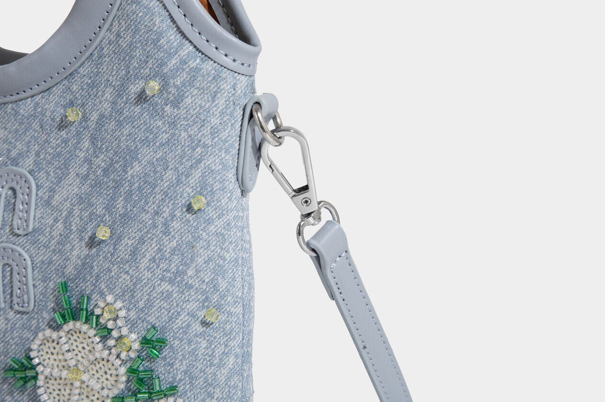 Kleine hellblaue Mini-Tote-Bag aus Stoff mit weißer Perlenblumenverzierung, runden Henkeln, silberfarbenen Beschlägen und