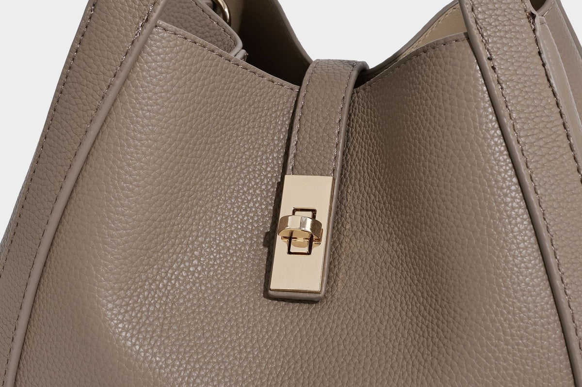 Structured trapezoid tote bag in taupe pebbled leather-look finish with gold-tone turn-lock hardware, dual top handles, and