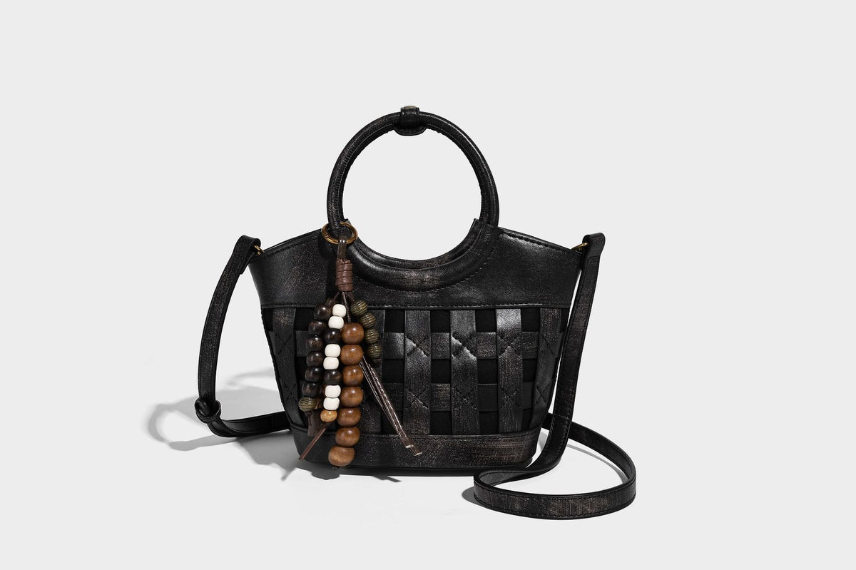 Small woven-panel bucket bag with circular ring handles, beaded tassel charm, and detachable crossbody strap in brown, detail