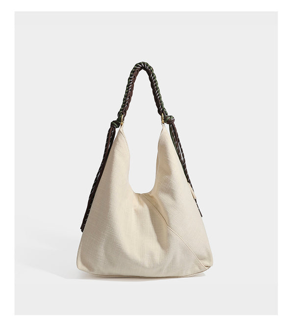 Soft slouchy cream canvas shoulder tote with braided brown and green cord handle, gold-tone ring hardware, and tassel trim