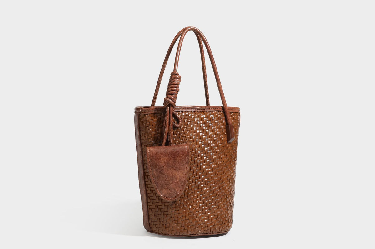 Structured woven-texture leather-look bucket bag in brown with knotted top handles, small front flap pouch, and adjustable