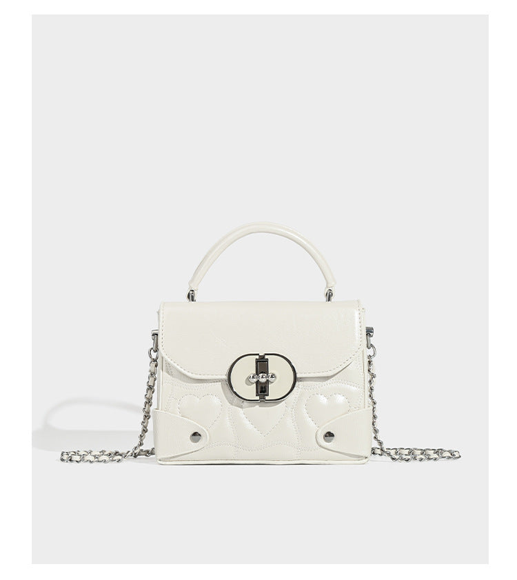 Kleine strukturierte Box-Tasche aus herzförmig gestepptem PU mit Henkel, silberfarbenem Kettenriemen zum Tragen als Crossbody und ovalem Drehverschluss, Detailansicht