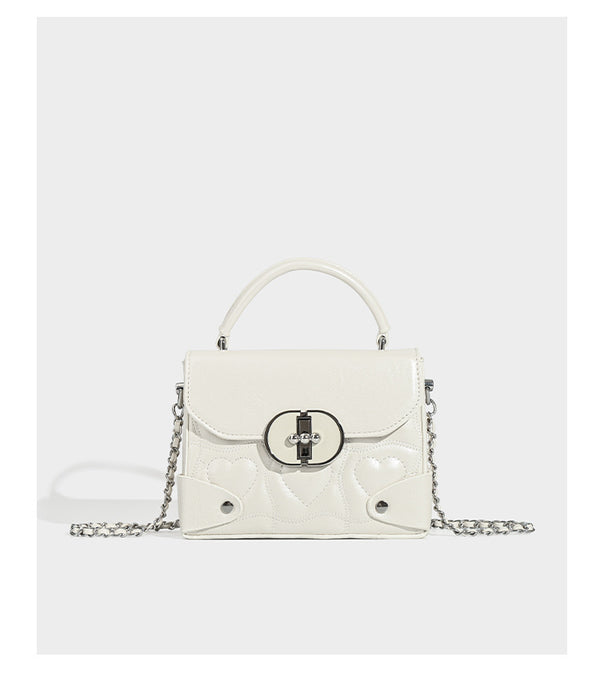 Kleine strukturierte Box-Tasche aus herzförmig gestepptem PU mit Henkel, silberfarbenem Kettenriemen zum Tragen als Crossbody und ovalem Drehverschluss, Detailansicht