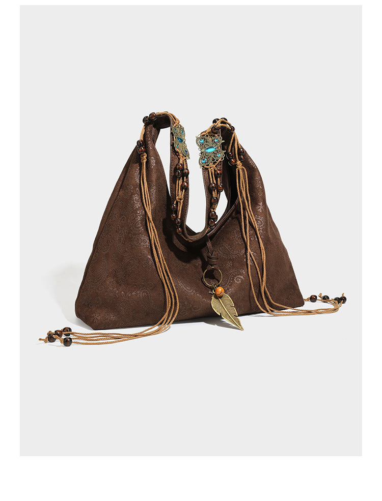 Slouchy boho hobo shoulder bag in embossed brown suede-look finish with beaded strap, cord tassels, and brass-tone leaf