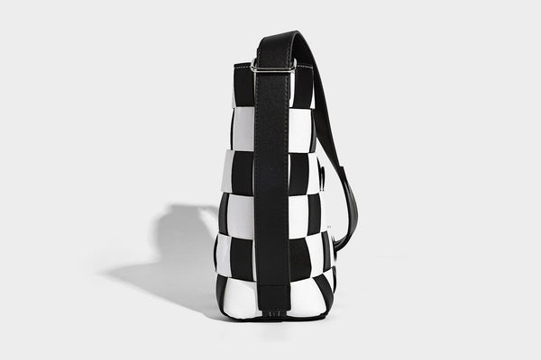 Hand-woven black-and-white checkerboard bucket bag with smooth black trim, silver-tone ring hardware, and adjustable