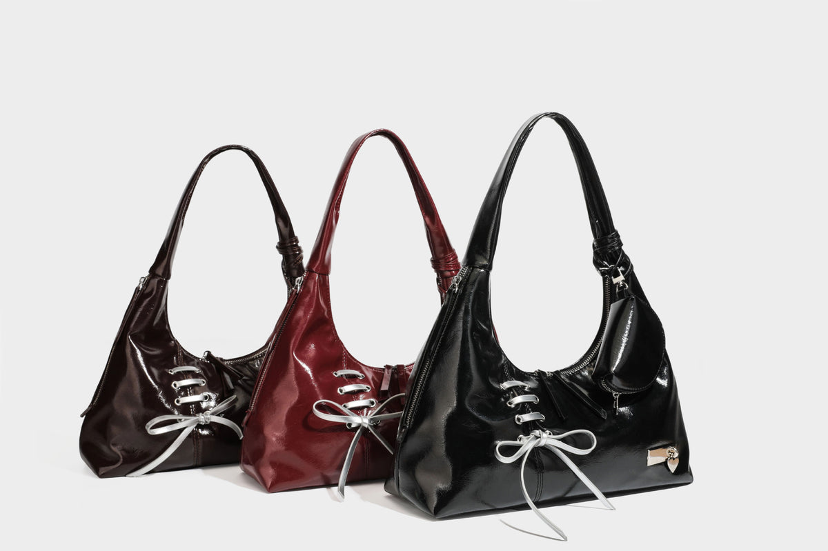 Weich fallende Hobo-Schultertasche in glänzender Lederoptik mit silberfarbenen Ösen zum Schnüren und Schleifenband auf der Vorderseite, Detailansicht