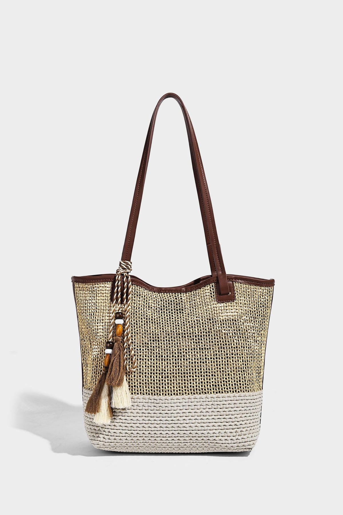 Woven beige and cream tote bag with brown leather-look trim, long double shoulder straps, and knotted tassel charm on front