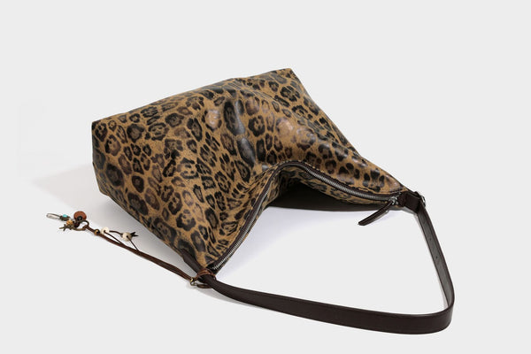 Slouchy leopard print hobo shoulder bag with glossy coated finish, top zipper closure, dark brown trim, and dangling charm