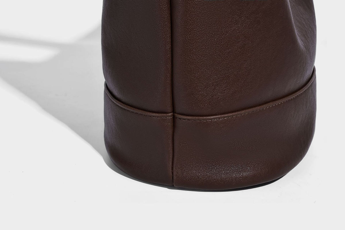 Slouchy bucket hobo shoulder bag in dark brown with glossy leather-look finish, top zip closure, and long adjustable, detail
