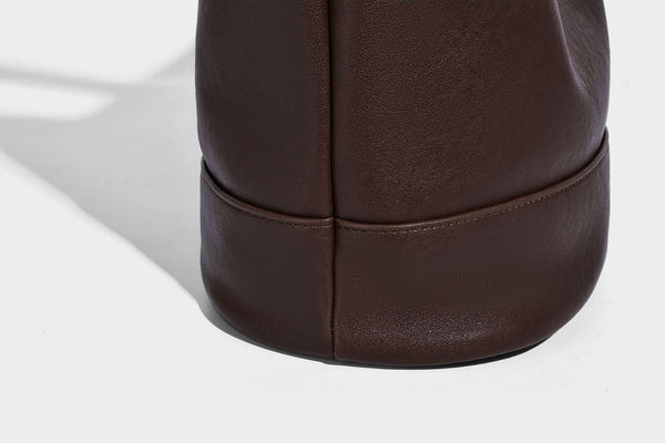 Slouchy bucket hobo shoulder bag in dark brown with glossy leather-look finish, top zip closure, and long adjustable, detail