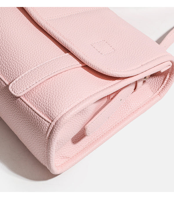 Compact structured flap satchel bag with pebbled texture, snap closure, front strap tabs, and long adjustable crossbody