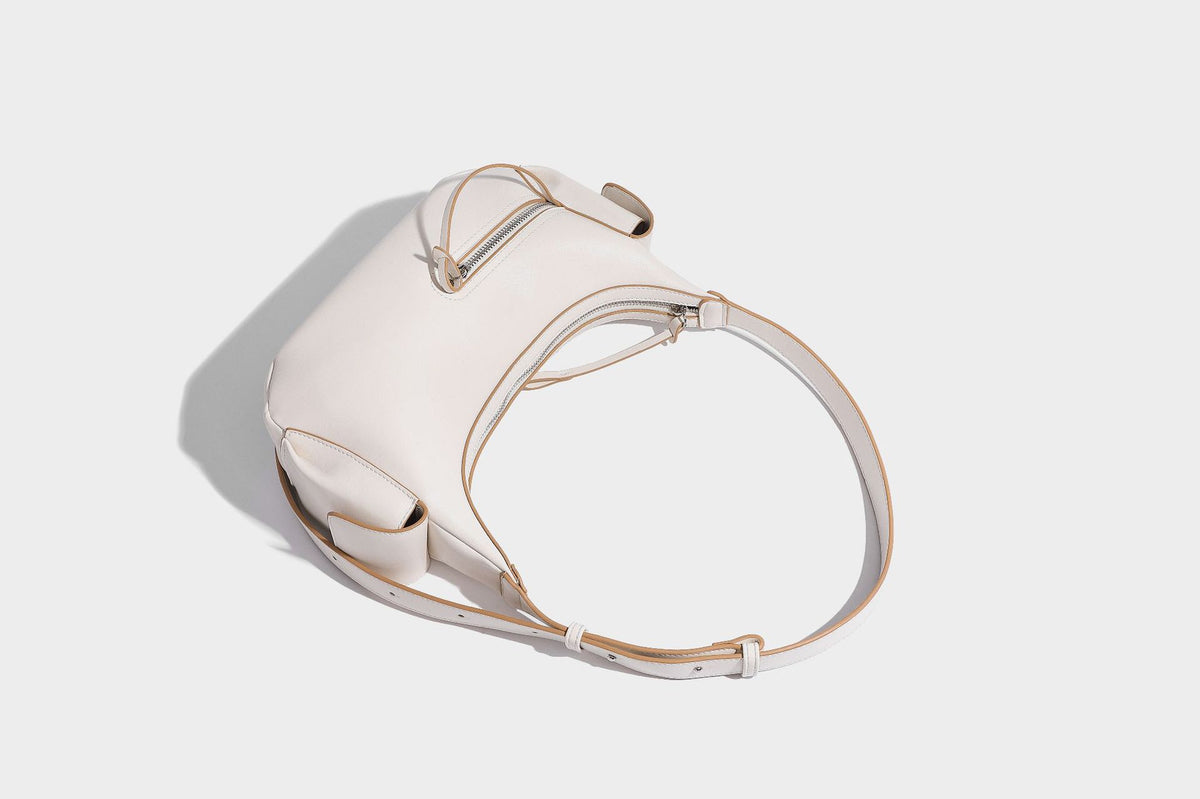 Smooth leather-look crescent shoulder bag with front zip pocket, side flap pockets, adjustable strap, and silver-tone, detail