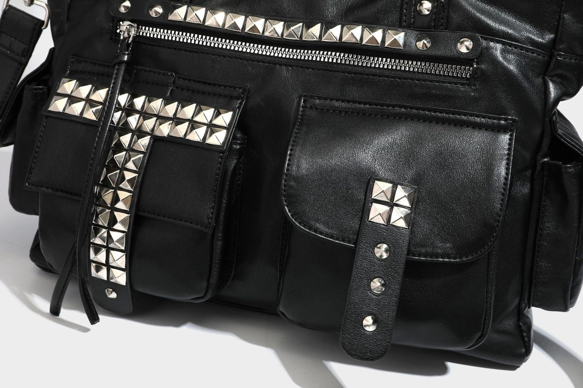 Black leather-look tote bag with silver pyramid studs on handles and front panel, multiple flap and zip exterior pockets