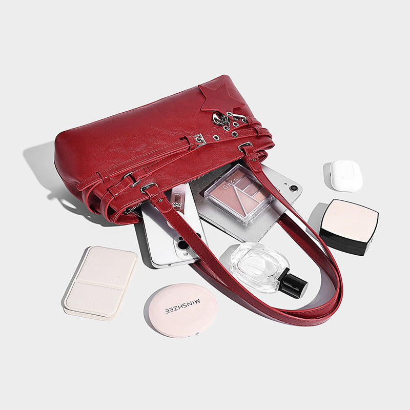 Structured glossy leather-look shoulder bag with wraparound belt straps, silver-tone hardware, and dangling star charm