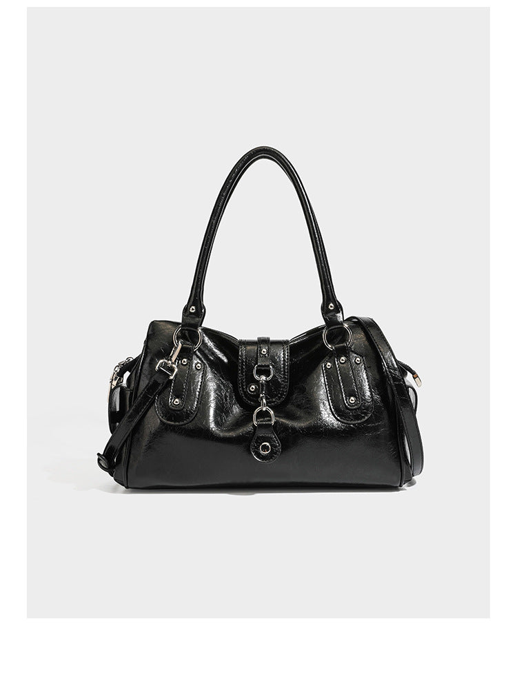 Glänzende, geknautschte Barrel-Satchel mit zwei oberen Tragegriffen, vorderem Klappen-Riemen-Panel, Ring- und Nietenbeschlägen sowie einem abnehmbaren