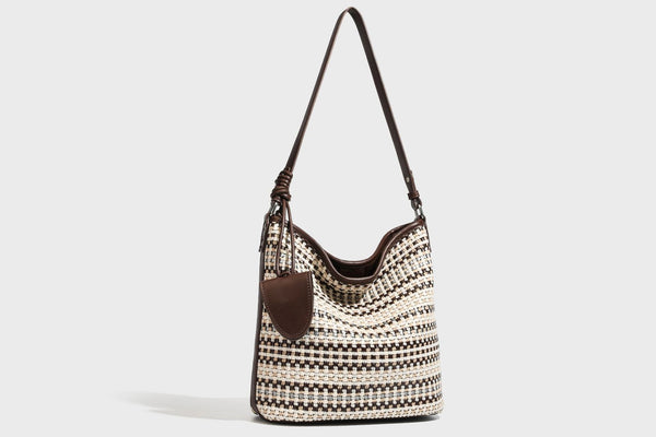 Woven stripe bucket shoulder bag in cream and dark brown with leather-look trim, knotted adjustable strap, and small shield