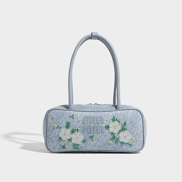 Small structured light blue denim-texture bowling bag with white floral bead embroidery, dual rounded top handles, and